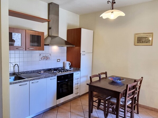 A compact kitchen with white cabinets, a gas stove, and a coffee maker. There is a dining table with chairs and a hanging light fixture.
