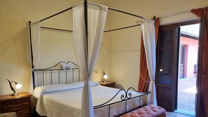 Un letto a baldacchino con tenda, una panca di legno, comodini con lampade e vista all'esterno da una porta.