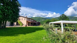 Una casa con giardino, un gazebo bianco e le montagne sullo sfondo.