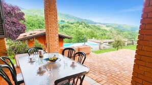 Un patio con tavolo e sedie, un muro in mattoni e vista su una piscina e montagne.