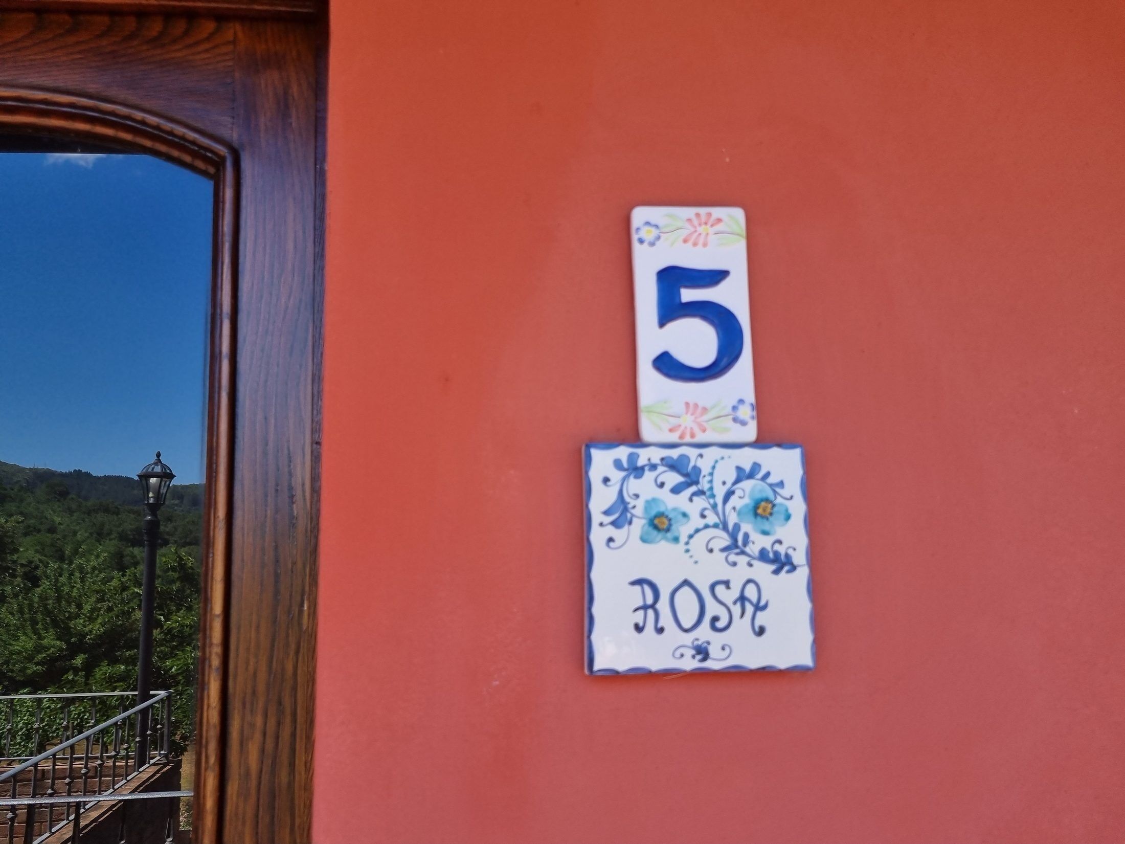 Un número de casa '5' y una placa con el nombre 'ROSA' en una pared roja.