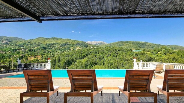 Una terrazza con quattro sedie di legno affacciata su una piscina e un paesaggio montuoso.