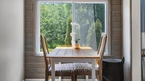 Een eetgedeelte met een houten tafel en stoelen, een raam met uitzicht op groen, en een potplant op de tafel.