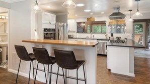 Een moderne keuken met een centraal kookeiland, barstoelen, roestvrijstalen apparatuur en hanglampen.