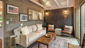 Een gezellige woonkamer met een houten plafond, een beige bank, een bijzettafeltje en een vloerkleed met dessin.