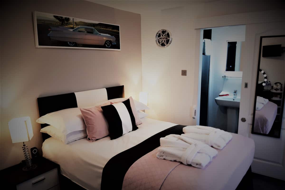 A hotel room with a bed, nightstands, a mirror, and a bathroom visible through an open door.