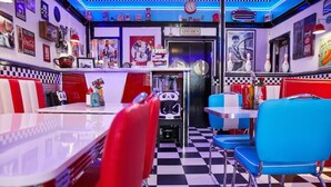 A diner with checkered flooring, red and blue booths, and a kitchen area.