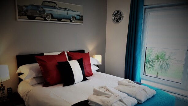 A neatly made bed with white and red pillows, a teal bedspread, and two white towels.