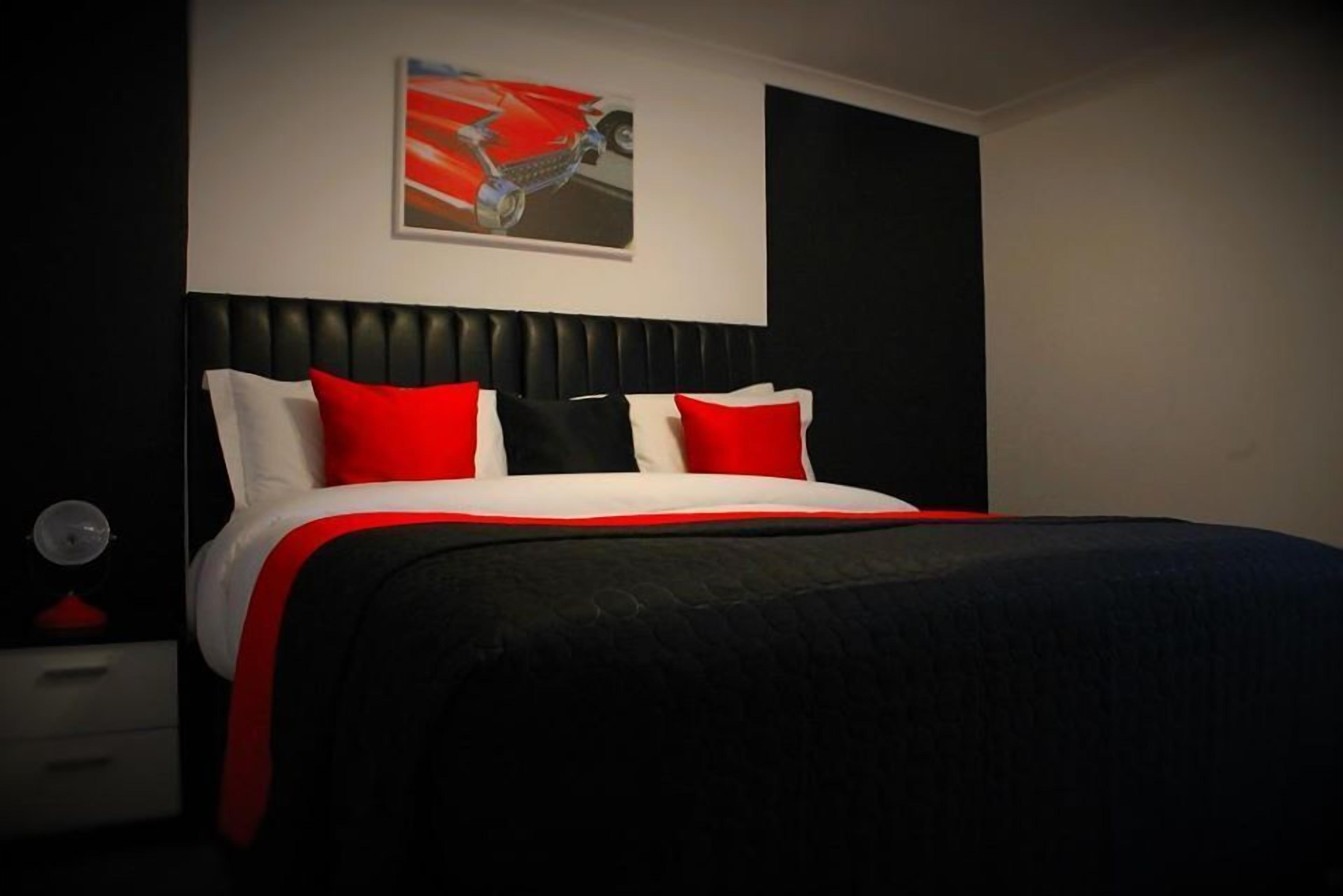 Un dormitorio moderno con cabecera negra, cama con ropa de cama roja y blanca, y una sola obra de arte en la pared.