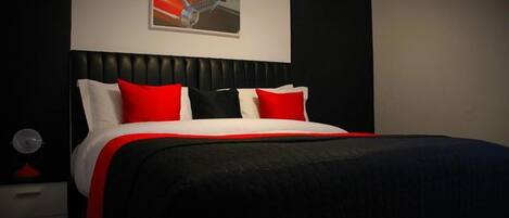 Un dormitorio moderno con cabecera negra, cama con ropa de cama roja y blanca, y una sola obra de arte en la pared.