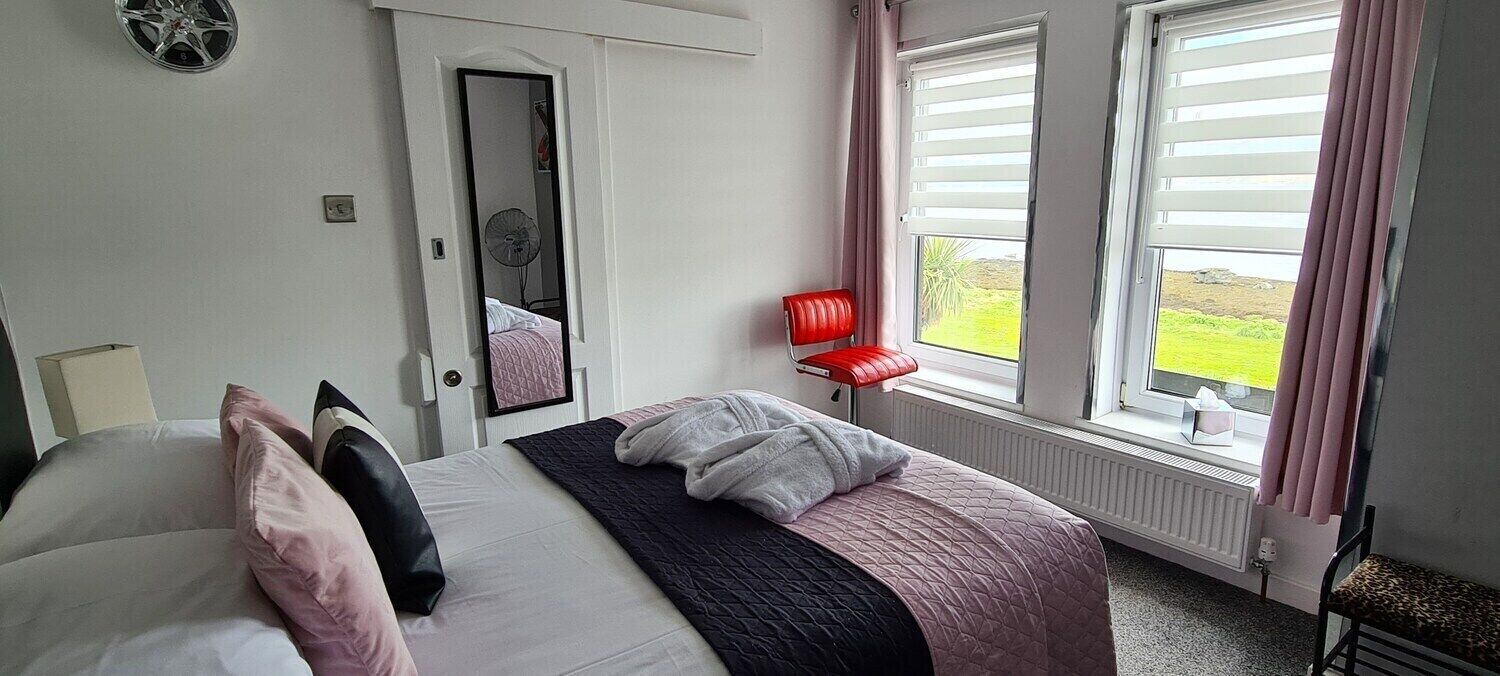 A bedroom with a bed, a red chair, a window with blinds, and a door leading to another room.