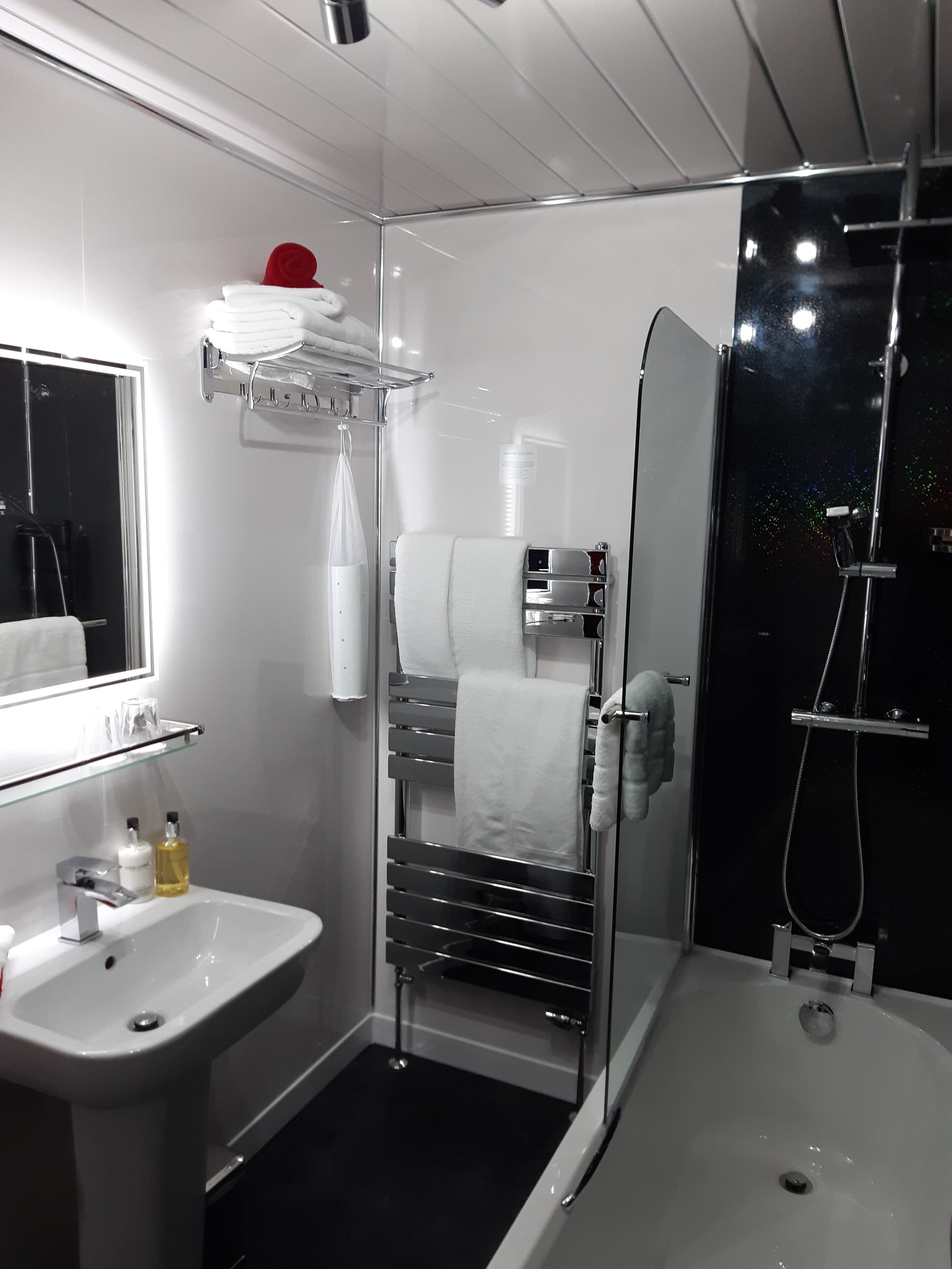 Un baño moderno con ducha de vidrio, lavamanos blanco y toallero con toallas dobladas.