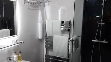 Un baño moderno con ducha de vidrio, lavamanos blanco y toallero con toallas dobladas.