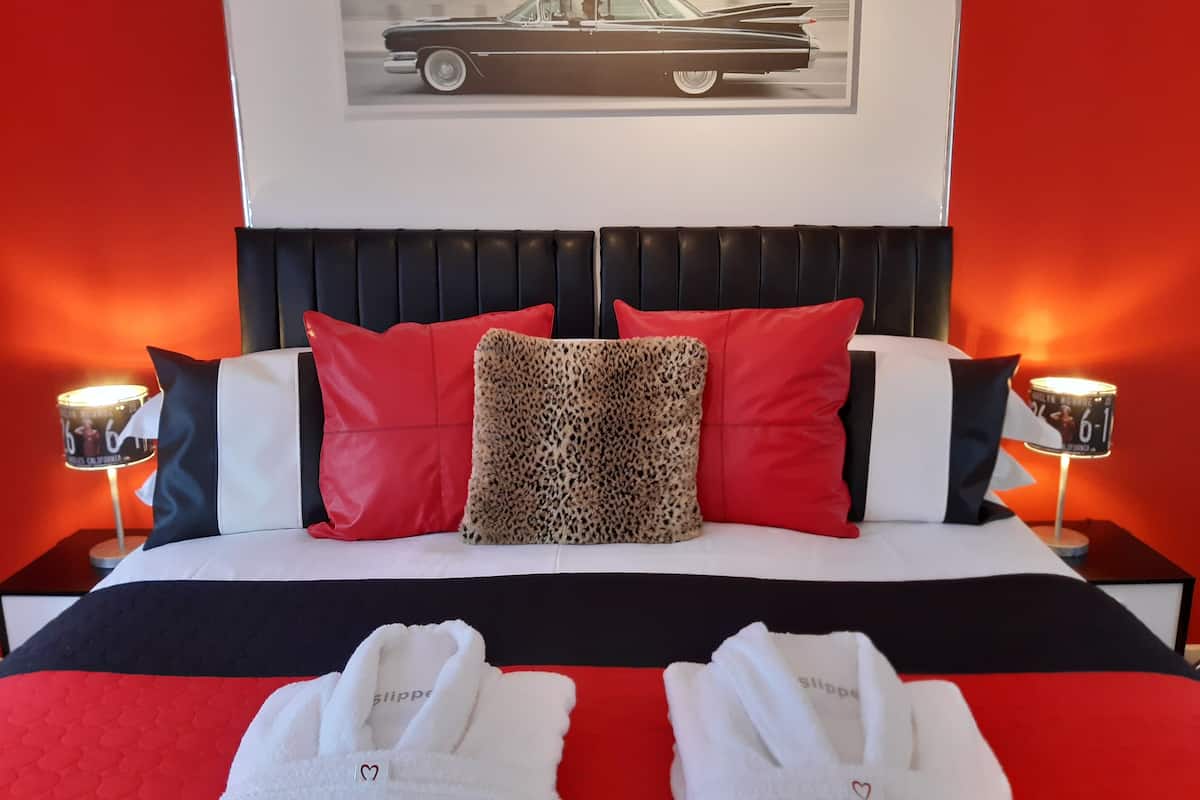 A bed with red and black bedding, two red pillows, a leopard print pillow, and two white towels with heart designs.