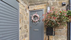 A stone wall exterior with a grey door, a doormat, and a potted plant.