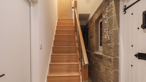 A wooden staircase with a handrail, leading to a room with a stone wall and a door with a number plate.