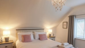 A neatly made bed with pillows, a bedside table with a lamp, a chandelier, and a window with curtains.