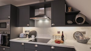 A modern kitchen with dark cabinetry, stainless steel appliances, and a marble countertop.