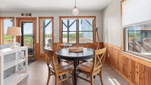 A dining area with a round table, wooden chairs, and a hanging light fixture. - Endless Summer: Direct Beach Access | Ocean Views (Duck)