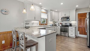 A modern kitchen with white cabinets, stainless steel appliances, and a granite countertop. - Endless Summer: Direct Beach Access | Ocean Views (Duck)