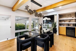 A modern dining area with a glass table, dark upholstered chairs, and a geometric ceiling light fixture.