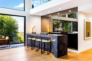 Een moderne keuken met een marmeren eiland, barkrukken en uitzicht op groen.