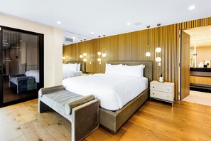 A modern hotel room with a large bed, bedside tables, a bench, and a view of the city.