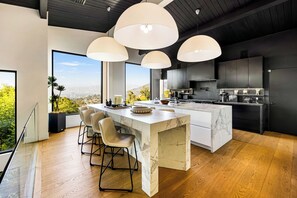 A modern kitchen with a marble island, pendant lighting, and a view of the city.