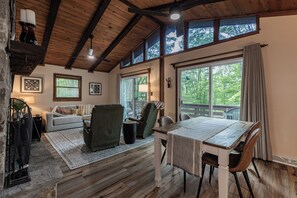 A cozy living room with a wooden ceiling, a dining table with chairs, a sofa, and a fireplace.