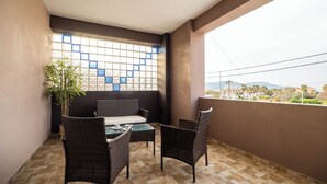A balcony with wicker furniture, a potted plant, and a view of distant buildings. - Semiso Beach Suite 9 (rethymno)