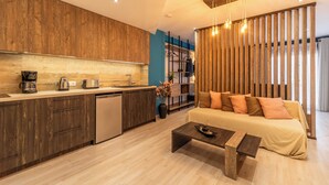 A modern kitchen with wooden cabinets, a built-in dishwasher, and a coffee maker. There is a sofa with cushions and a coffee table in the living area. - Semiso Beach Suite 9 (rethymno)