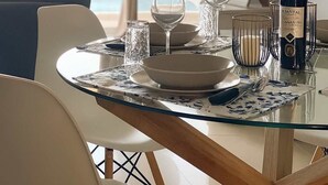 A dining area with a glass table, white chairs, and a bottle of Esential wine. - Seafront Kalamata Haven - Blue Luxury Suite (Kalamata)