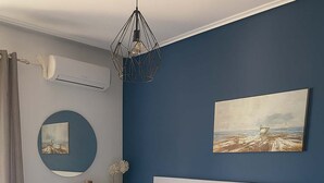 A modern bedroom with a large bed, bedside tables, a reading chair, and a wall-mounted air conditioner. - Seafront Kalamata Haven - Blue Luxury Suite (Kalamata)