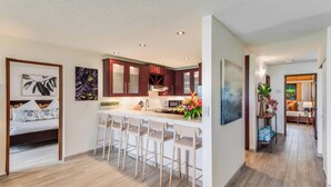 A modern kitchen with a central island, bar stools, and a dining area with a sofa and lamp.