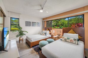 Ein Hotelzimmer mit zwei Betten, einem Fernseher, einem Deckenventilator und einem großen Fenster mit Blick auf Bäume.