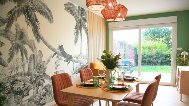 A dining area with a tropical mural, wooden table, red chairs, and a view of greenery outside.