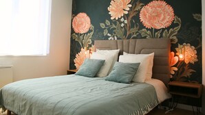 A bedroom with a large bed, two bedside tables, and a wall with floral wallpaper.