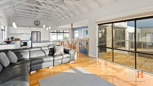 A modern living room with a black leather sofa, wooden flooring, and a large sliding glass door leading to a balcony. - Sea La Vie, King Bed, Sleeps 7 (Cowes)