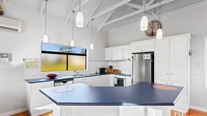 A modern kitchen with white cabinets, a central island with stools, pendant lighting, and a large window with a view. - Sea La Vie, King Bed, Sleeps 7 (Cowes)