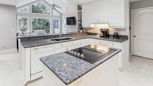 Cozinha moderna com ilha central, armários brancos e uma janela ampla com vista para o exterior.