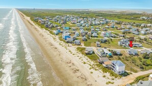 Vue aérienne d’une zone résidentielle côtière, avec des maisons le long de la plage, un ciel dégagé et une vue lointaine sur l’océan.