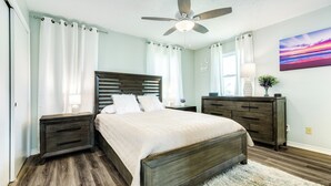 Une chambre à coucher avec un lit en bois, des tables de chevet, une commode, un ventilateur de plafond et un tableau accroché au mur.