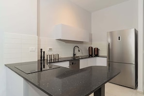 Uma cozinha moderna com bancada preta, eletrodomésticos de aço inoxidável e armários brancos.