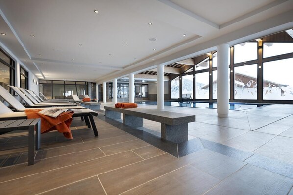 A spacious indoor area with sun loungers, a stone bench, and large windows offering a view of the outdoors.