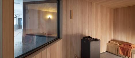 A sauna room with wooden walls, a large window, a sauna heater, and a wooden bench.