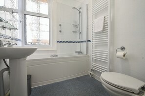 Un baño con lavamanos blanco, bañera, inodoro y ventana.