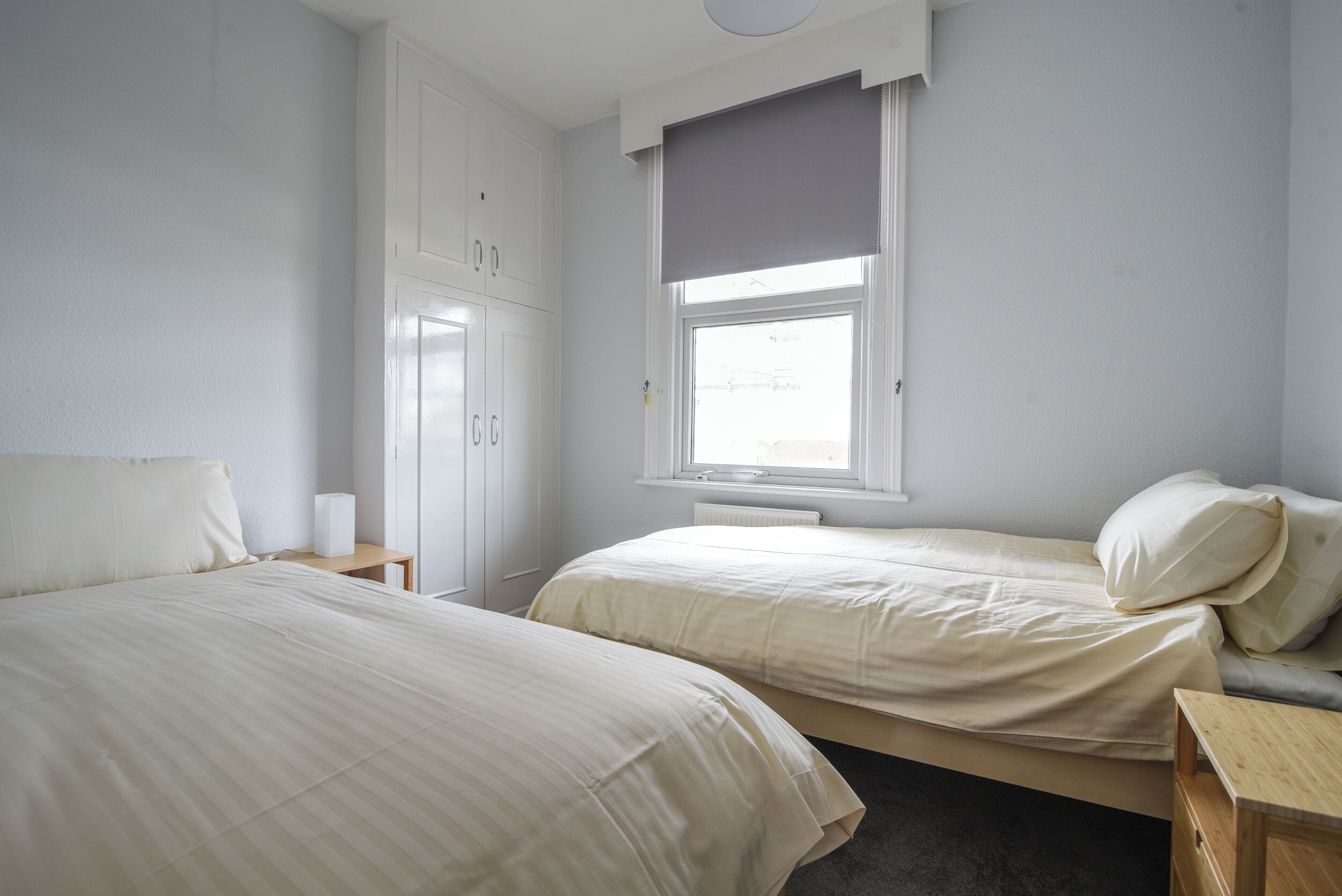 Ein Schlafzimmer mit zwei Betten, einem Kleiderschrank, einem Fenster mit Jalousie und einem Nachttisch.