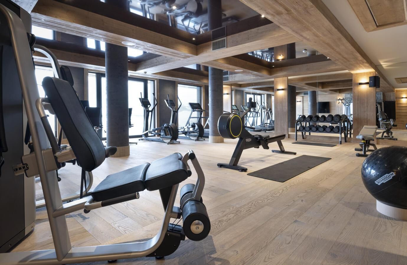 Une salle de sport équipée de matériel d’exercice, dotée de planchers en bois et de grandes fenêtres.