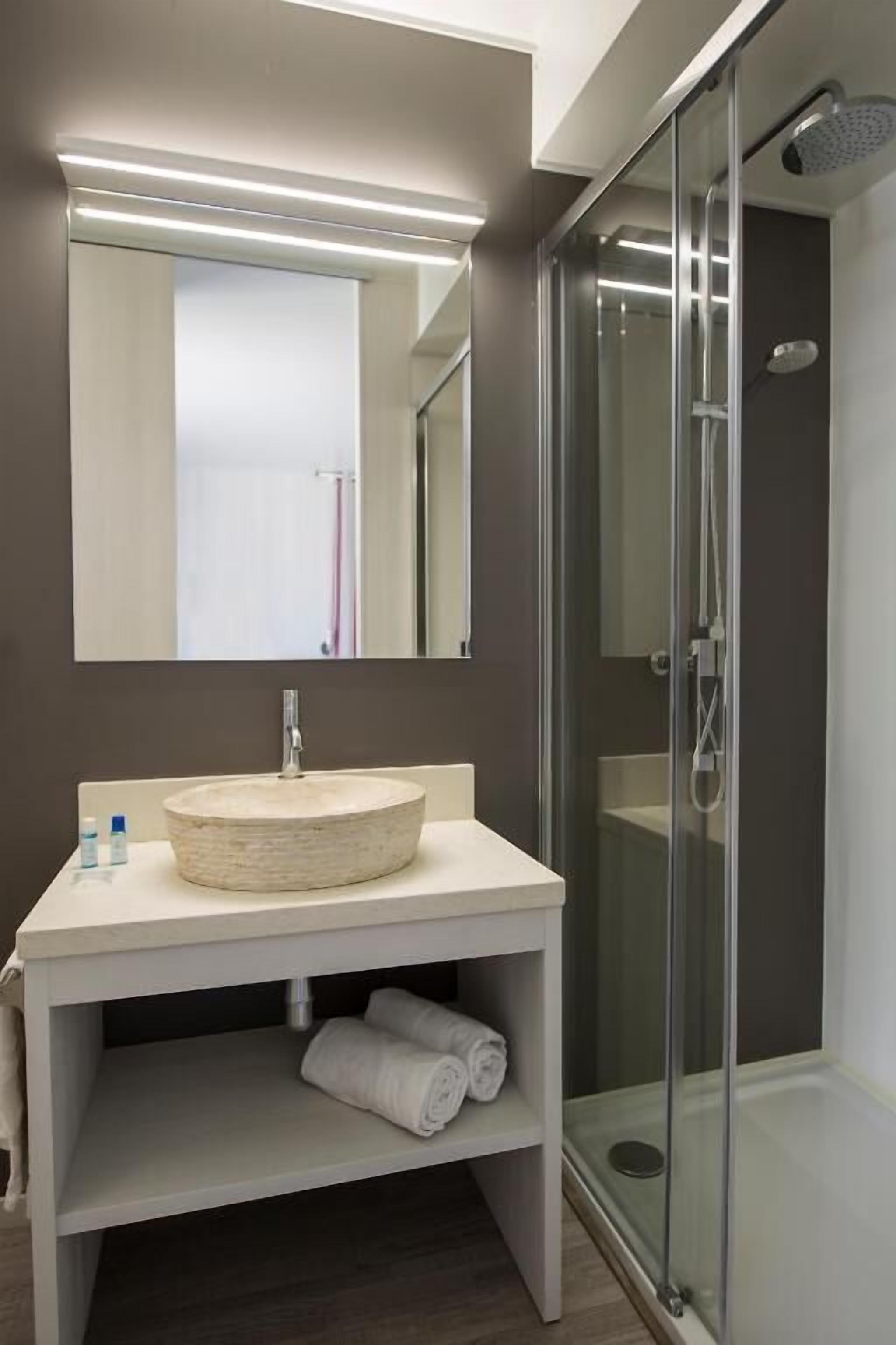 A modern bathroom with a round sink, a mirror, and a glass-enclosed shower.