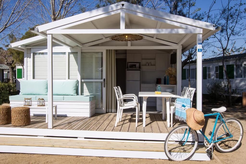 A covered outdoor area with a white bench, a table, and chairs. A bicycle is parked nearby.
